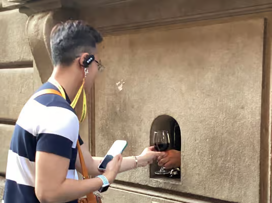Traveler collecting a glass of red wine from a traditional Florence wine window, a unique stop on florence wine tours.