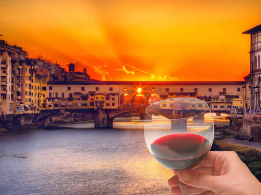 Glass of red wine held at sunset overlooking Ponte Vecchio and the Arno River in Florence, a scenic highlight of florence wine tours.