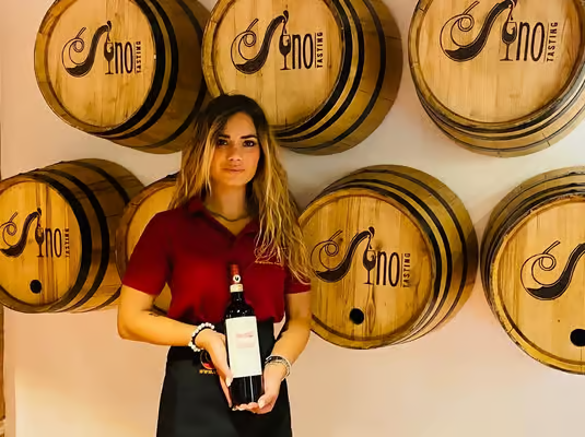 Winery staff member holding a bottle of Tuscan red wine in front of oak barrels, part of authentic tastings on florence wine tours.