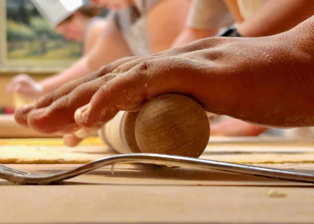 Close-up of hands rolling fresh pasta dough with a wooden pin during a hands-on culinary workshop, authentic preparation experience featured in the best venice cooking classes