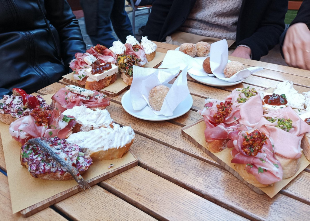 Colorful Venetian cicchetti including cured meats, creamy cheeses, seafood spreads, and small pastries served on wooden boards at an outdoor bacaro table, capturing authentic tasting culture featured on Venice Food And Wine Tours.