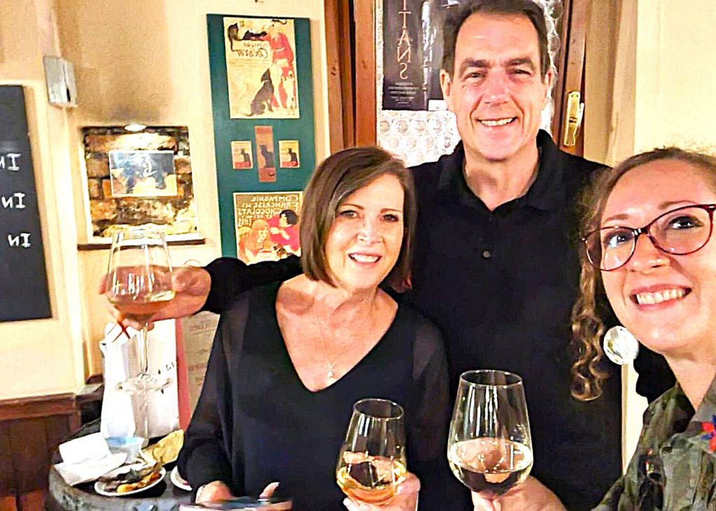 Smiling travelers holding glasses of local Venetian wine inside a cozy wine bar, capturing the social atmosphere, tastings, and cultural experience commonly enjoyed during Venice Food And Wine Tours.