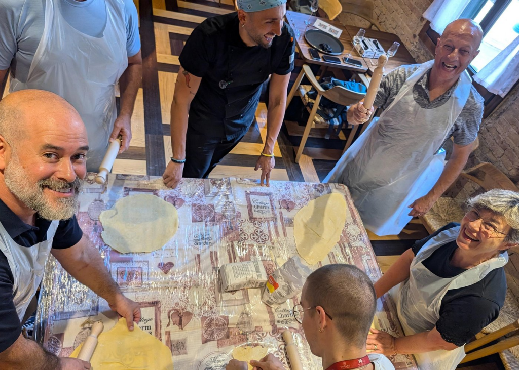 Group of travelers gathered around a kitchen table rolling fresh pasta dough during a Venetian cooking class, guided by a local chef, capturing the interactive culinary experiences often included in Venice Food And Wine Tours.