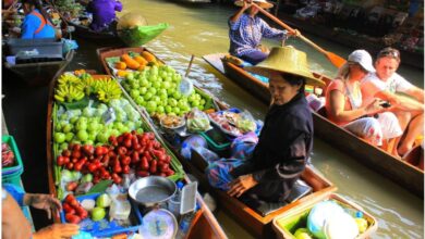 Bangkok Tours experience at a floating market with vendors selling fresh fruit and local food from wooden boats while visitors explore the canals.