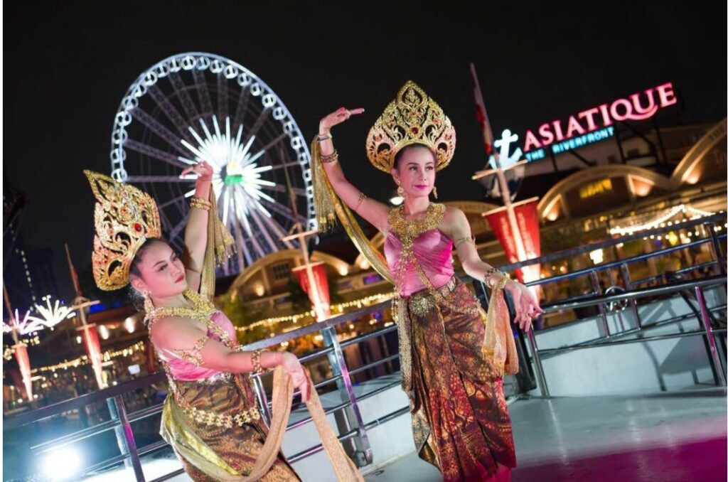 Thai cultural dancers performing on a dinner cruise Bangkok experience near Asiatique The Riverfront with the Ferris wheel illuminated at night
