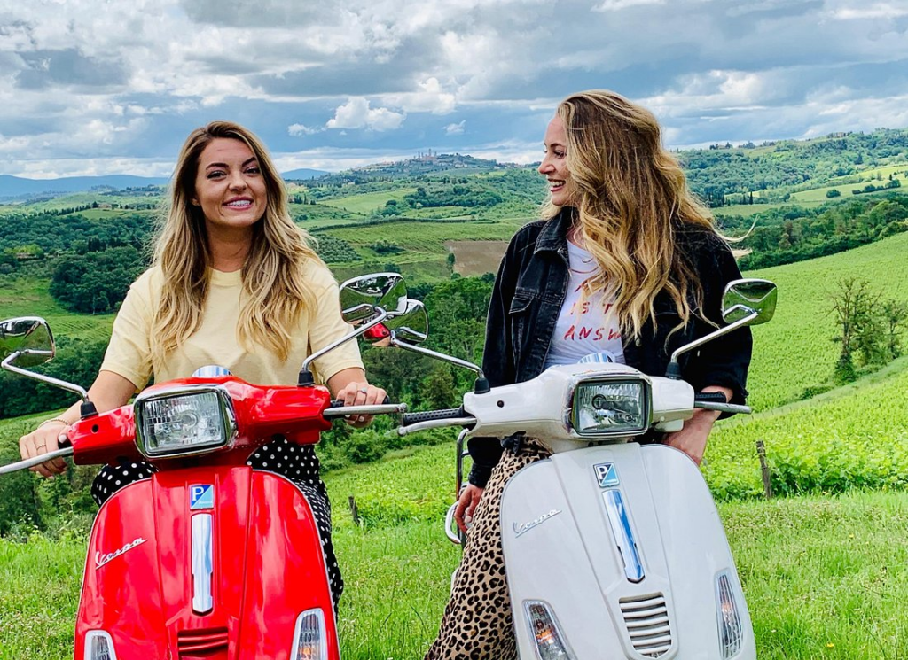 Two women pausing with their Vespas overlooking Tuscan vineyards on a vespa wine tour florence