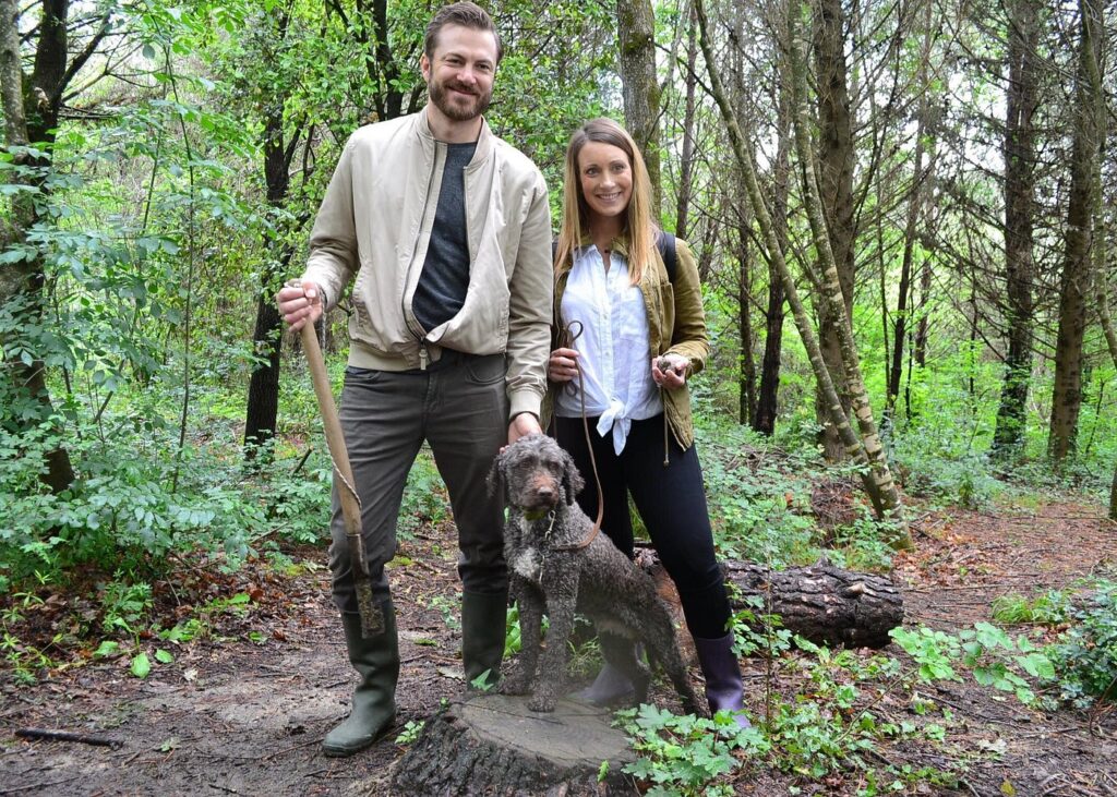 Couple with trained dog and shovel during truffle hunting Florence experience in a Tuscan forest.