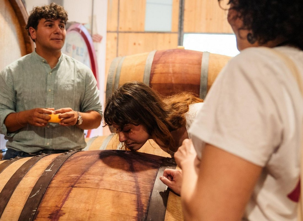 Visitors smelling wine aging in oak barrels during a winery visit on tuscany wine tours from rome, guided through the cellar for an authentic tasting experience.