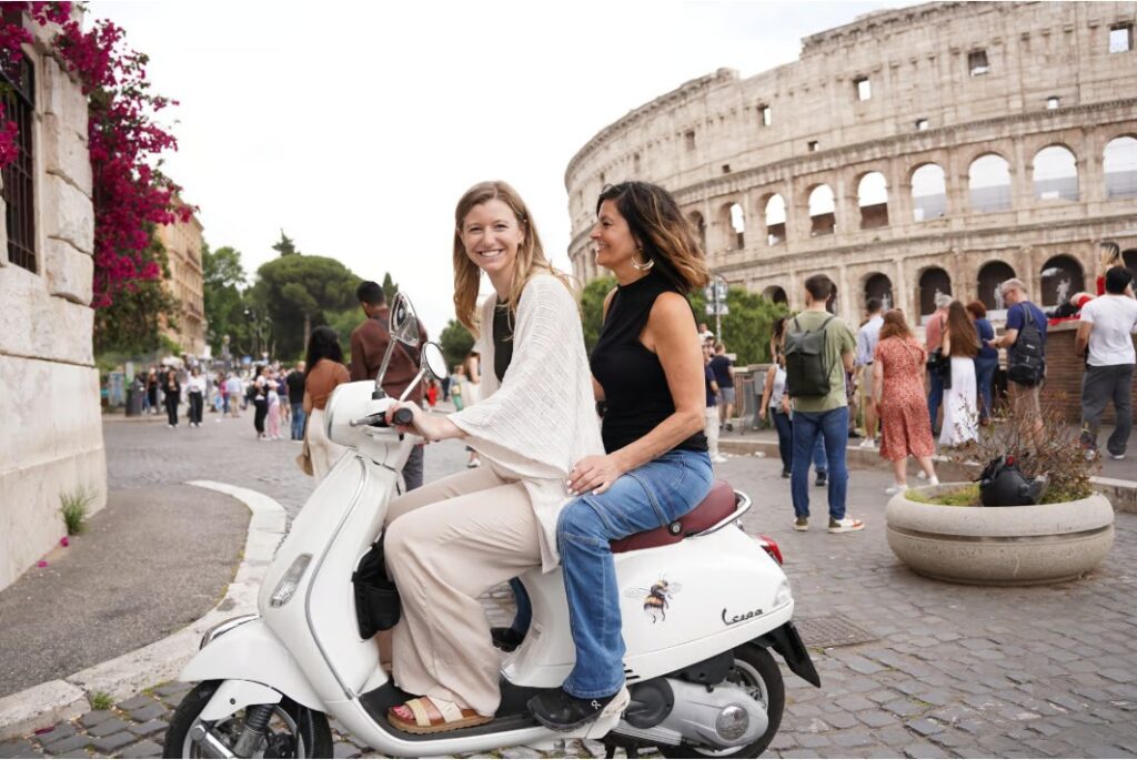 Two women riding a Vespa near the Colosseum during a Rome Vespa Food Tour