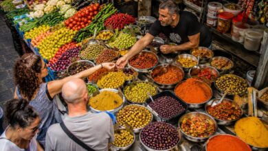 Colorful spice bowls, olives and fresh produce at a busy Tel Aviv market stall during one of the best Israel food and market tours.