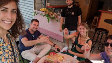 Carmel Market Tel Aviv food tour with travelers enjoying fresh fruit shots and local tastings at a vibrant market cafΓ© surrounded by vendors and neighborhood eateries.
