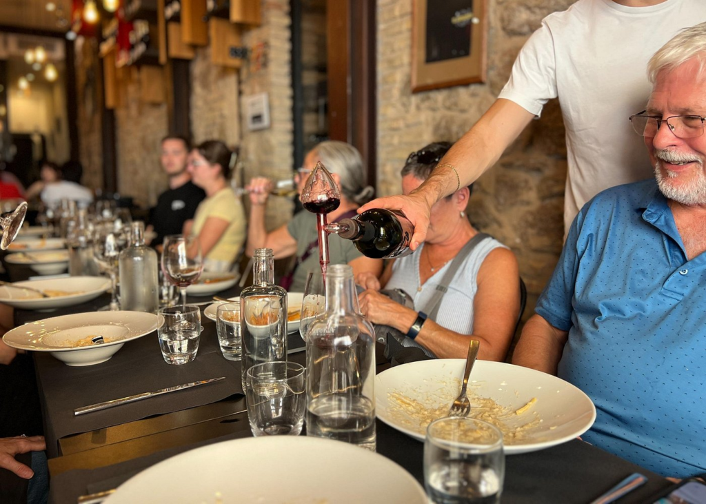 Rome food and wine tours featuring guests enjoying a guided Italian wine tasting as a server pours red wine during a shared dining experience in a traditional Roman restaurant.