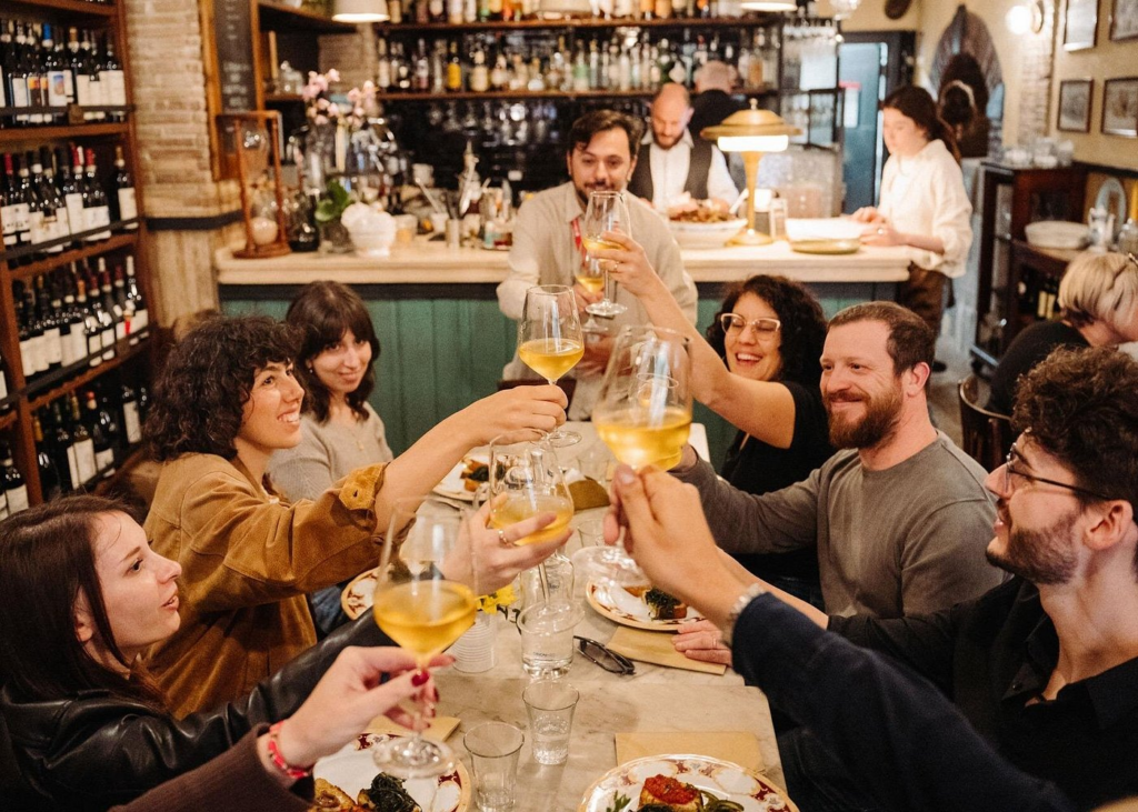 Rome food and wine tours with travelers raising glasses of Italian white wine during a lively group tasting inside a traditional Roman wine bar and restaurant.