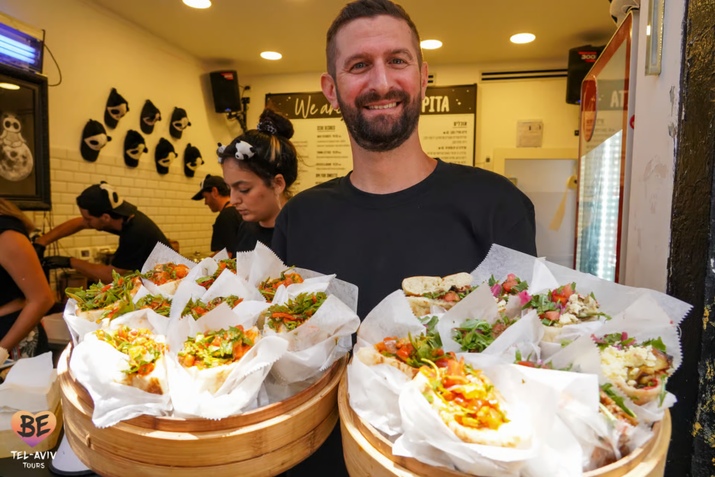 Carmel Market Tel Aviv featuring a local vendor serving freshly made gourmet pita sandwiches filled with vibrant Israeli salads and seasonal ingredients at a popular market eatery.