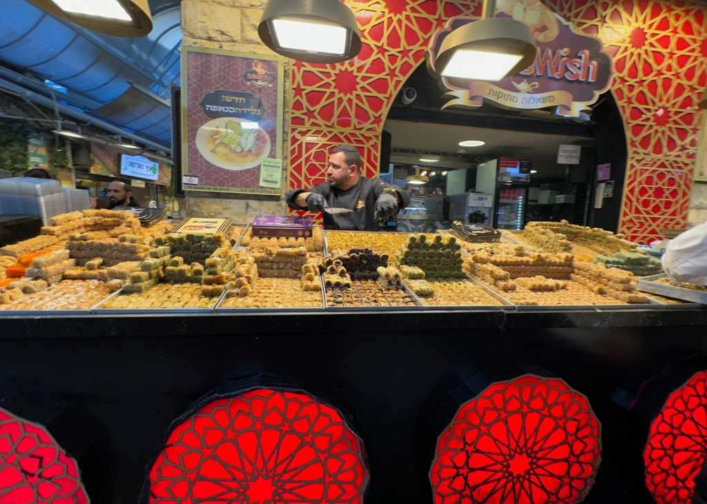 Baklava and Middle Eastern pastries on display at a bustling market sweet shop, a delicious stop on Israel food and market tours.