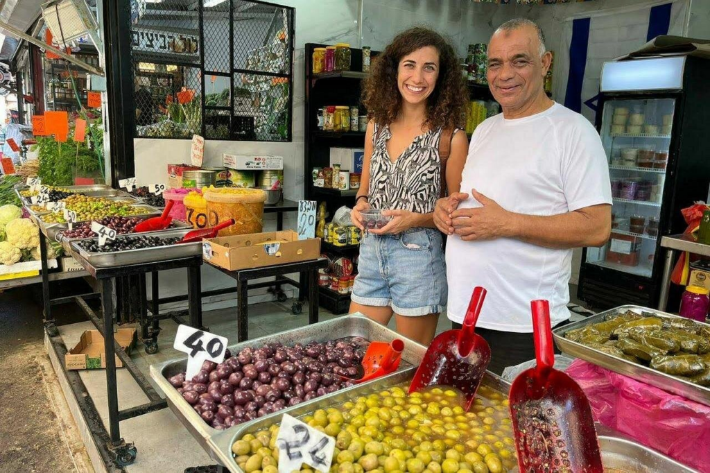Guide and local vendor sampling olives and market specialties at Tel Aviv's Carmel Market on one of the best Israel food and market tours.