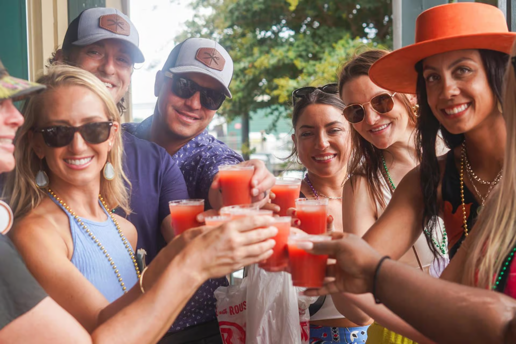 Friends raising colorful cocktails together during a New Orleans cocktail tour, celebrating in the lively French Quarter.