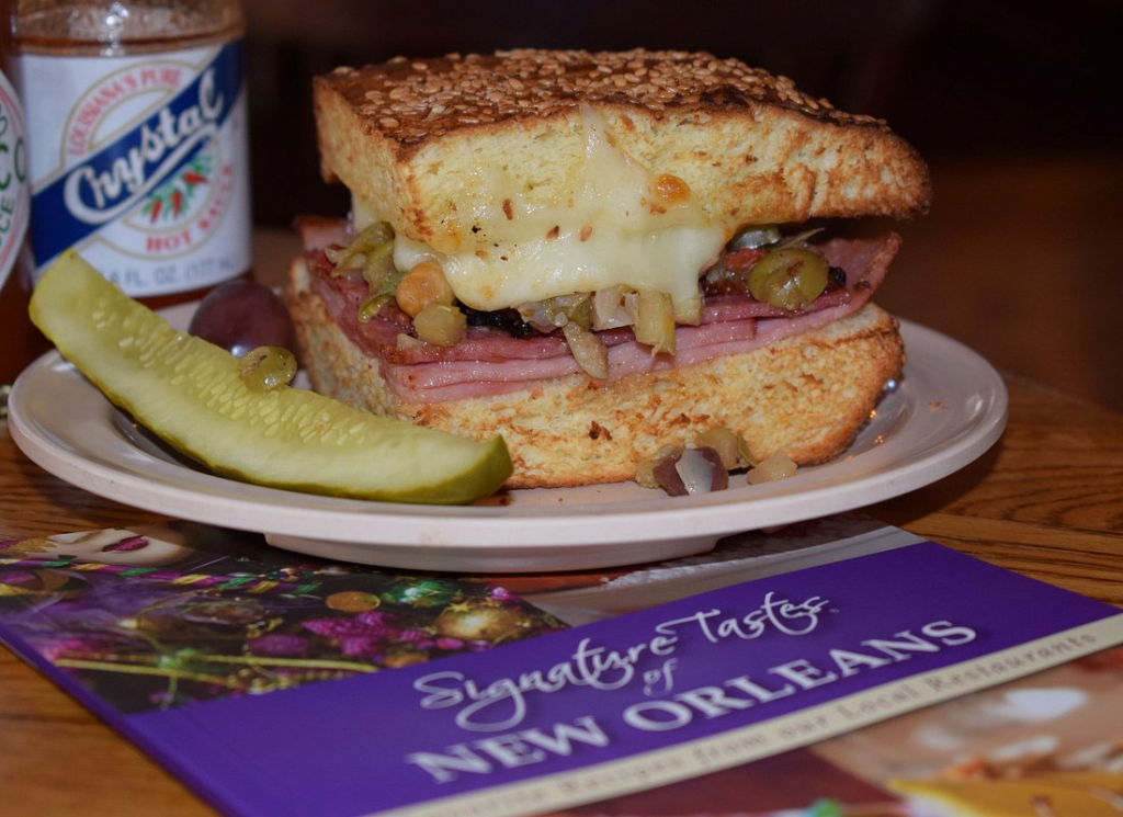 Classic New Orleans muffuletta sandwich with layers of ham, salami, melted cheese, and olive salad, featured on the best food tours in New Orleans.