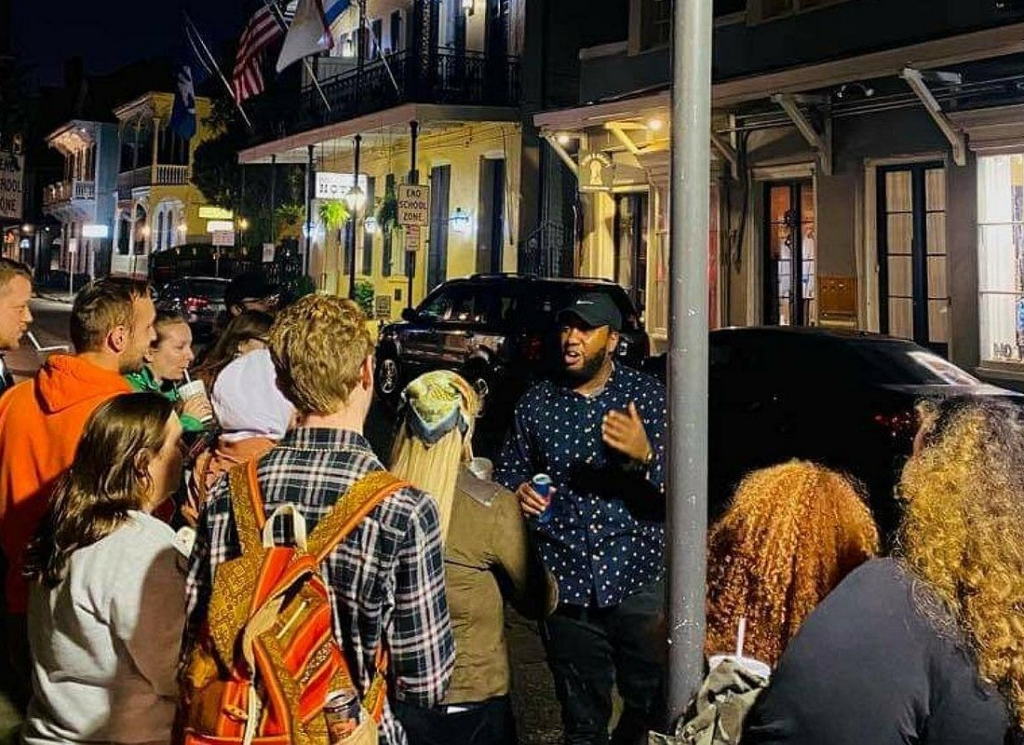 Haunted pub crawl New Orleans with a guide telling chilling ghost stories to a group gathered on a historic French Quarter street at night.