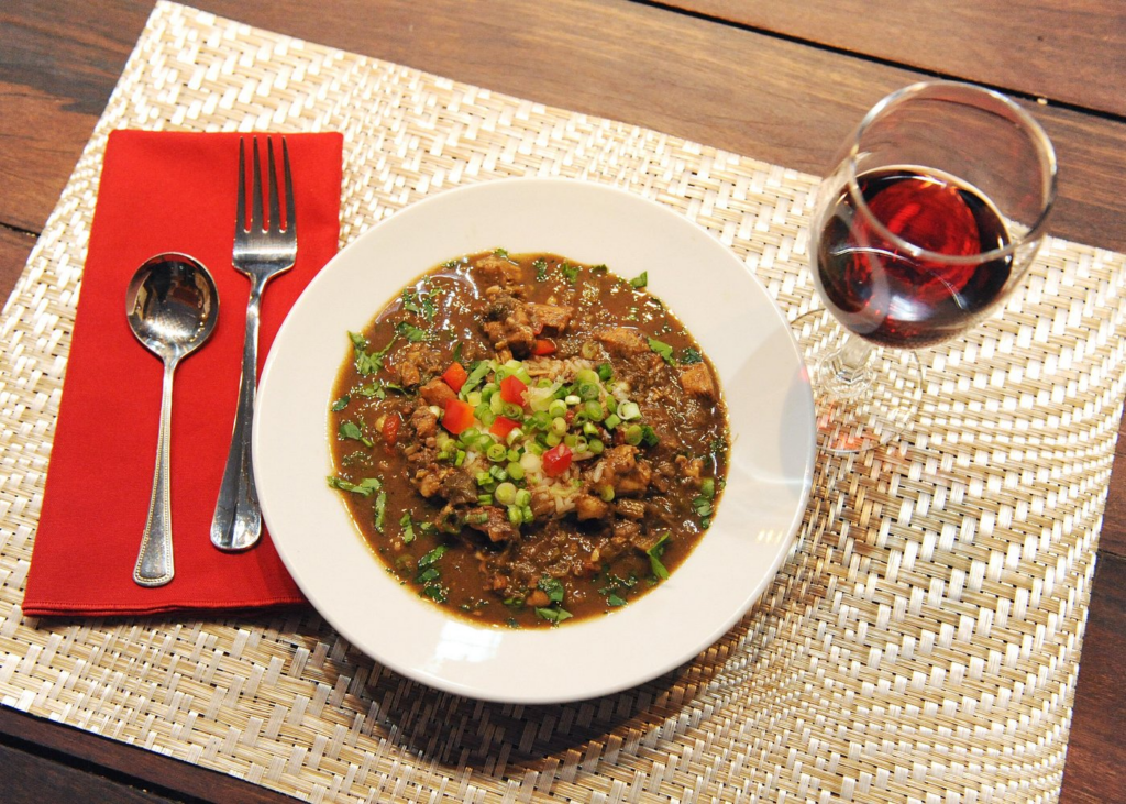 A bowl of authentic Cajun gumbo served over rice with a glass of wine during a cooking class New Orleans experience.