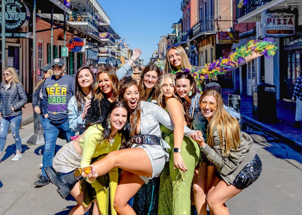 Friends celebrating on Bourbon Street during a lively New Orleans pub crawl, posing for photos amid colorful balconies, festive Mardi Gras beads, and the vibrant French Quarter atmosphere.