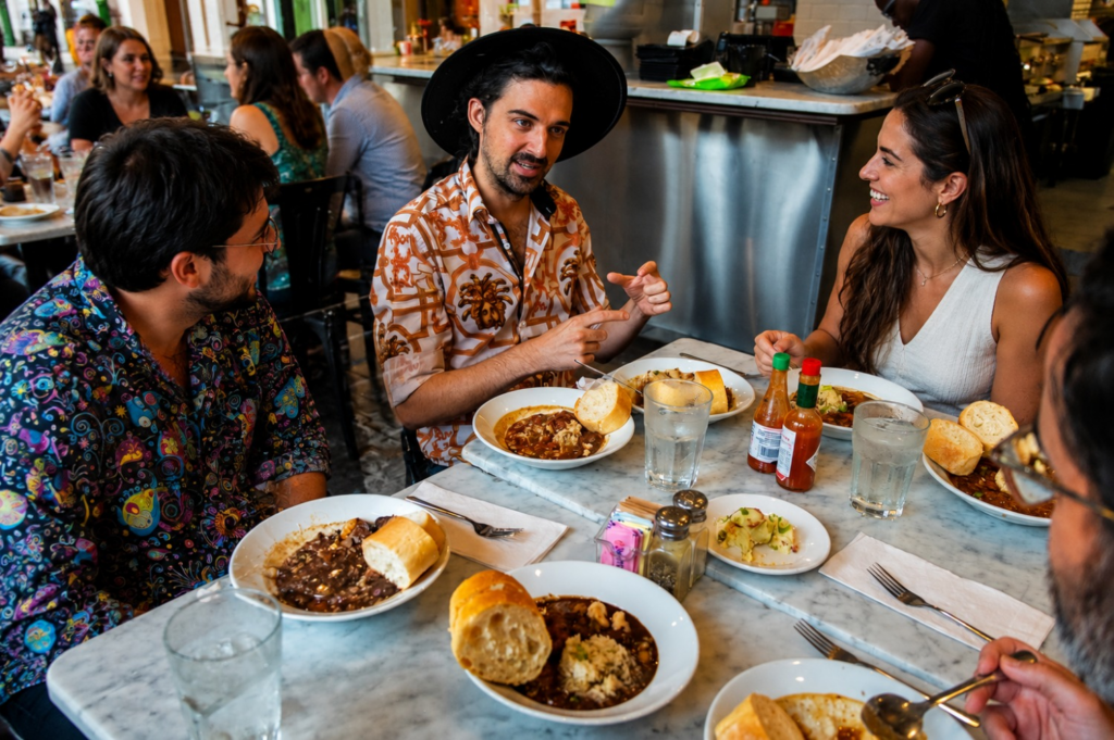 A guide shares stories over bowls of gumbo as guests enjoy local dishes during a French Quarter food tour at a lively New Orleans restaurant.